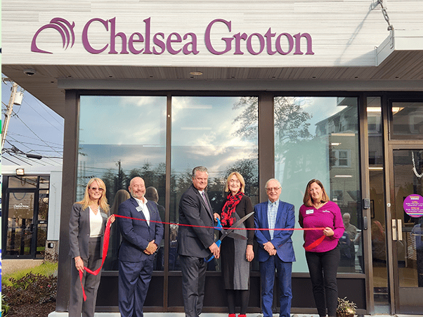 3 men and 3 women in business attire hold a red ribbon in front of Chelsea Groton Bank