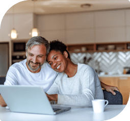 A man and woman sitting and smiling looking at their saving account on a laptop