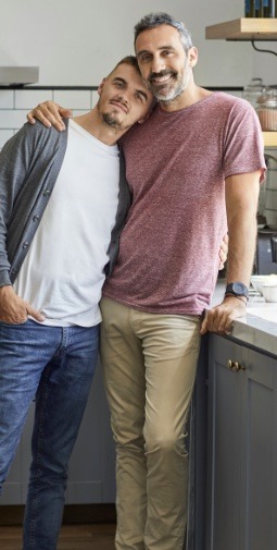 A man rests his head on the shoulder of another man who leans on a counter