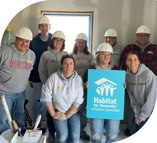 Nine volunteers with white hardhats hold a blue habitat for humanity of Eastern Connecticut sign